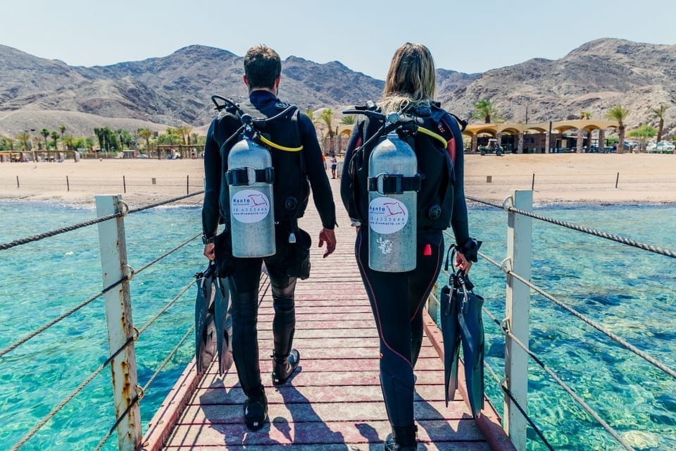 two divers with diving gear walking on a bridge on the coral nature reserve